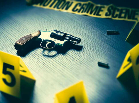 A revolver on a table surrounded by evidence markers and caution tape