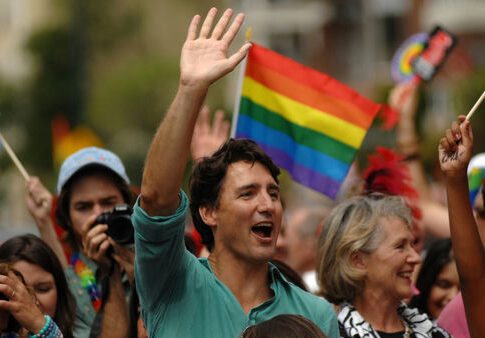 Man waving in a crowd with a rainbow flag in the background