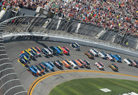 NASCAR race at Daytona Speedway with cheering spectators.