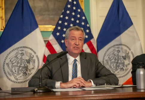 Man speaks at a press conference with flags behind.