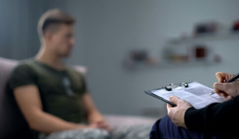 Therapist taking notes while talking with a young man.