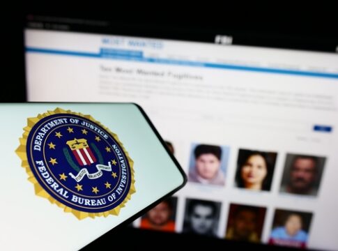 FBI logo displayed on a smartphone with a website showing wanted individuals in the background
