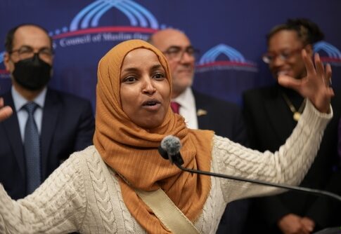 Ilhan Omar speaking passionately at a podium with a group of supporters behind her