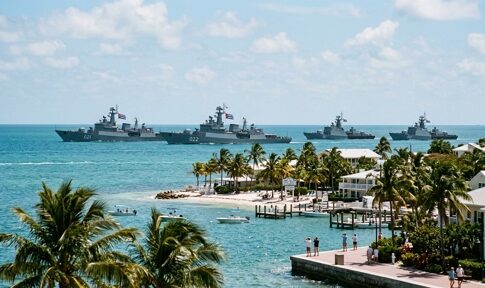 A fleet of naval ships sailing in the ocean near a tropical shore